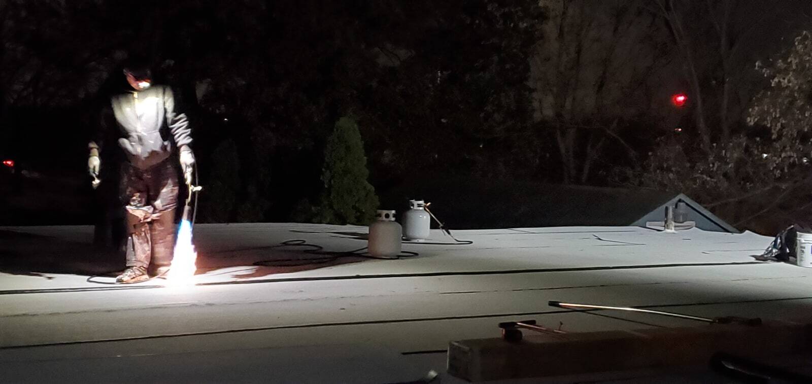 Ryan applying roofing membrane on a flat roof at night